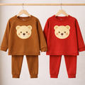 Two children's pajama sets, one brown and one red, with bear face designs on hangers against a neutral background.