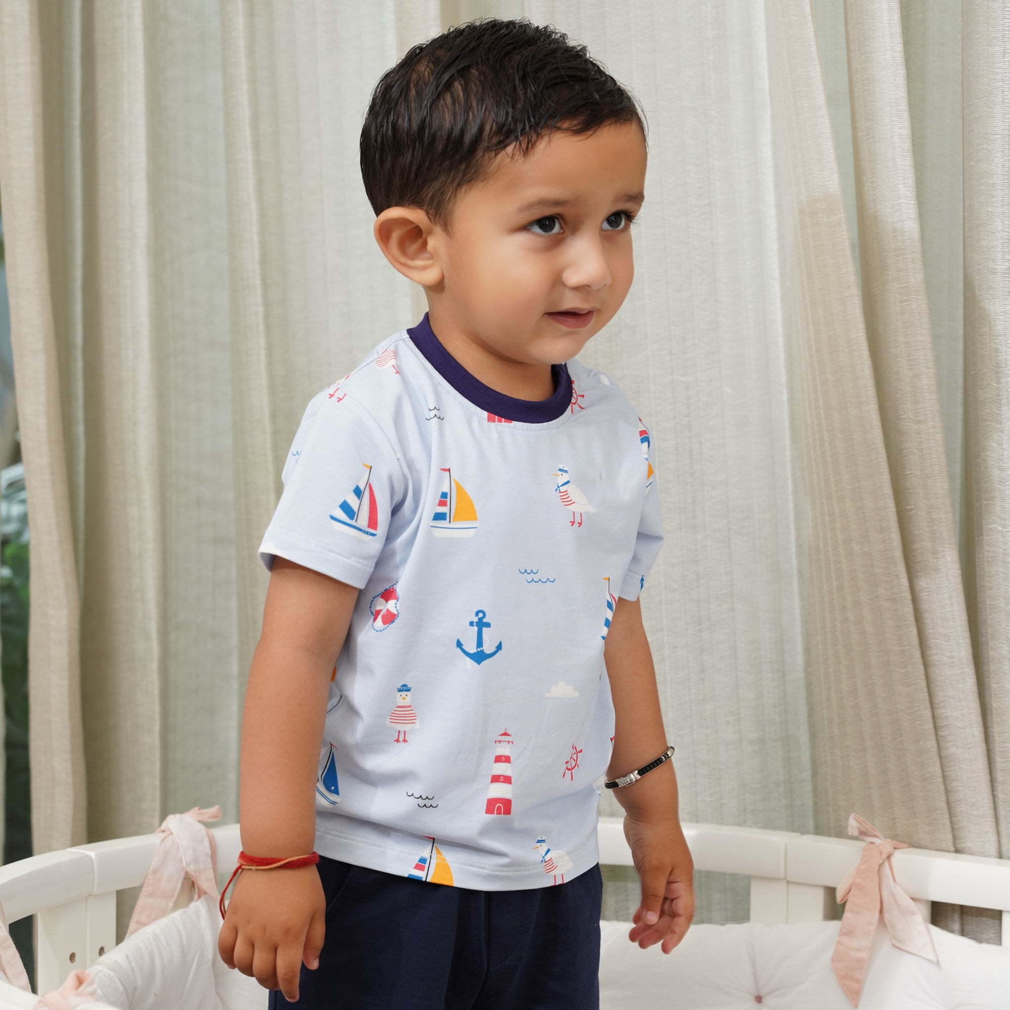 Child wearing a light bamboo gray t-shirt with colorful patterns standing in front of beige curtains.