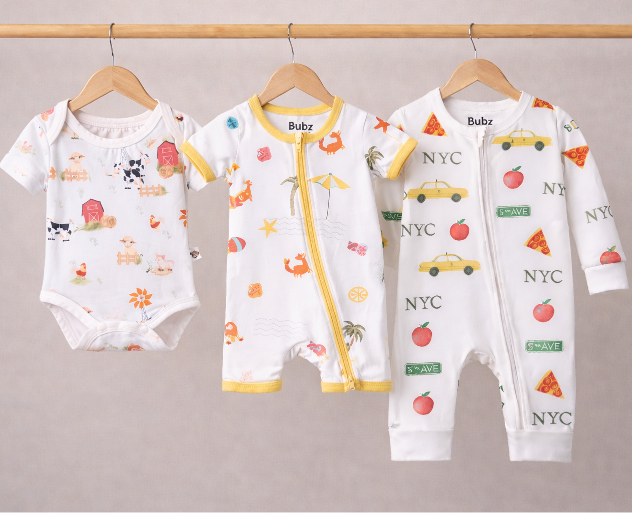 Three baby rompers with various prints on hangers against a plain background