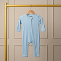 Light blue baby bamboo onesie hanging on a wooden hanger against a beige paneled wall.