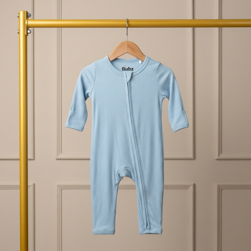 Light blue baby bamboo onesie hanging on a wooden hanger against a beige paneled wall.
