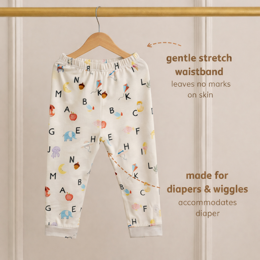 Children's bamboo pants with alphabet pattern on a hanger against a beige wall.