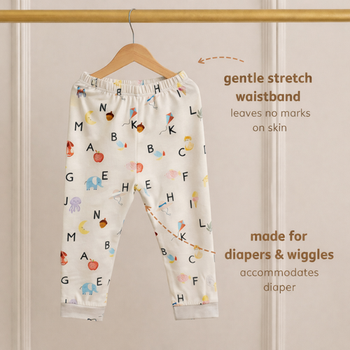 Children's bamboo pants with alphabet pattern on a hanger against a beige wall.
