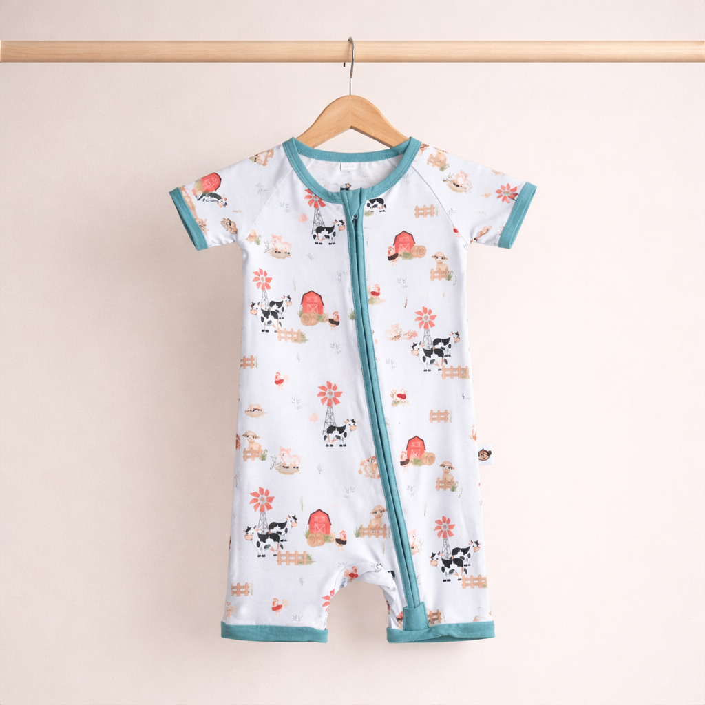Baby romper with farm animal pattern on a hanger against a beige background