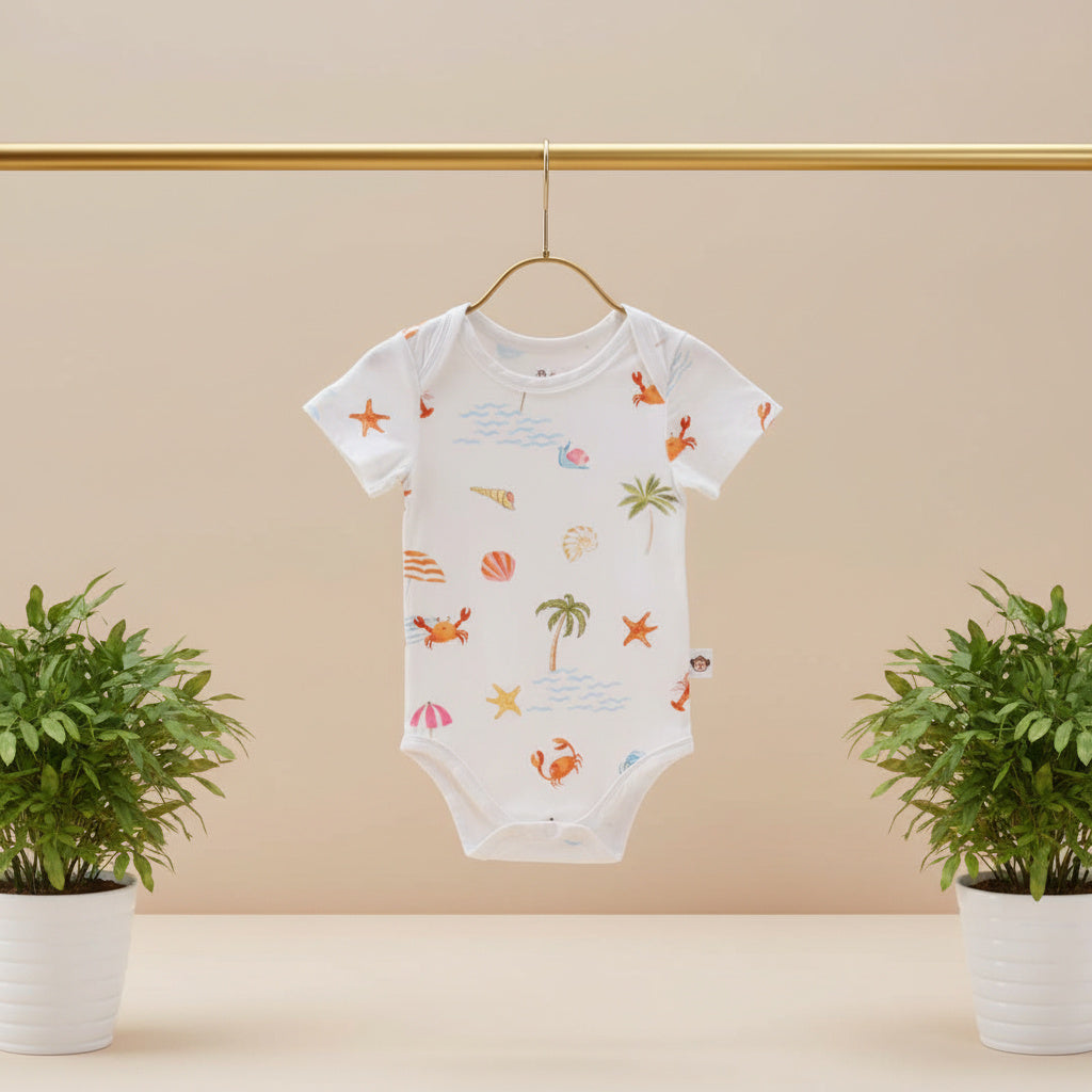 Baby onesie with a beach-themed pattern hanging on a gold rod against a beige wall with two potted plants.
