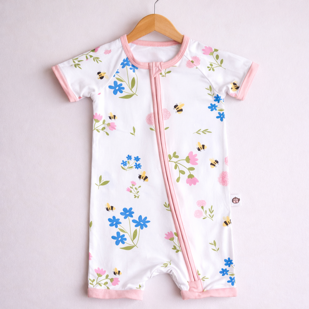 Baby romper with floral and bee pattern on a hanger against a light pink background