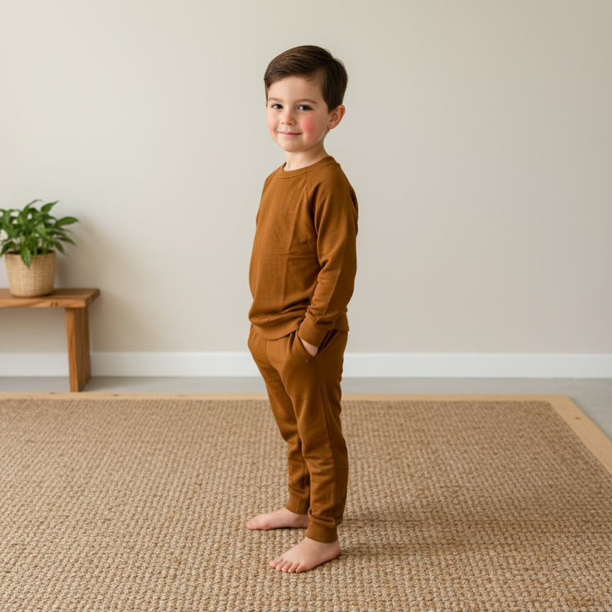 Child wearing a brown outfit standing on a woven mat in a minimalistic room.
