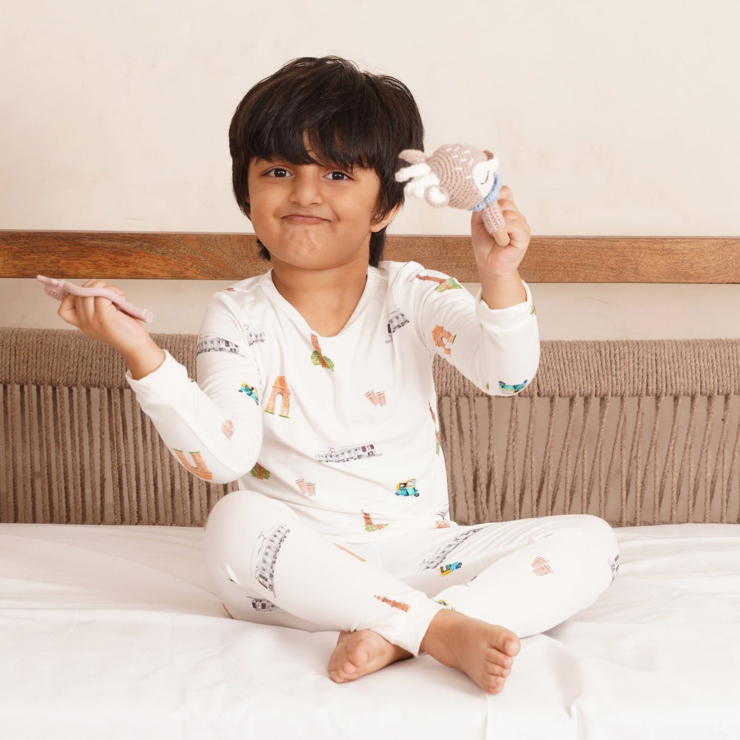 Child in bamboo pajamas sitting on a bed holding a toy, with a neutral background