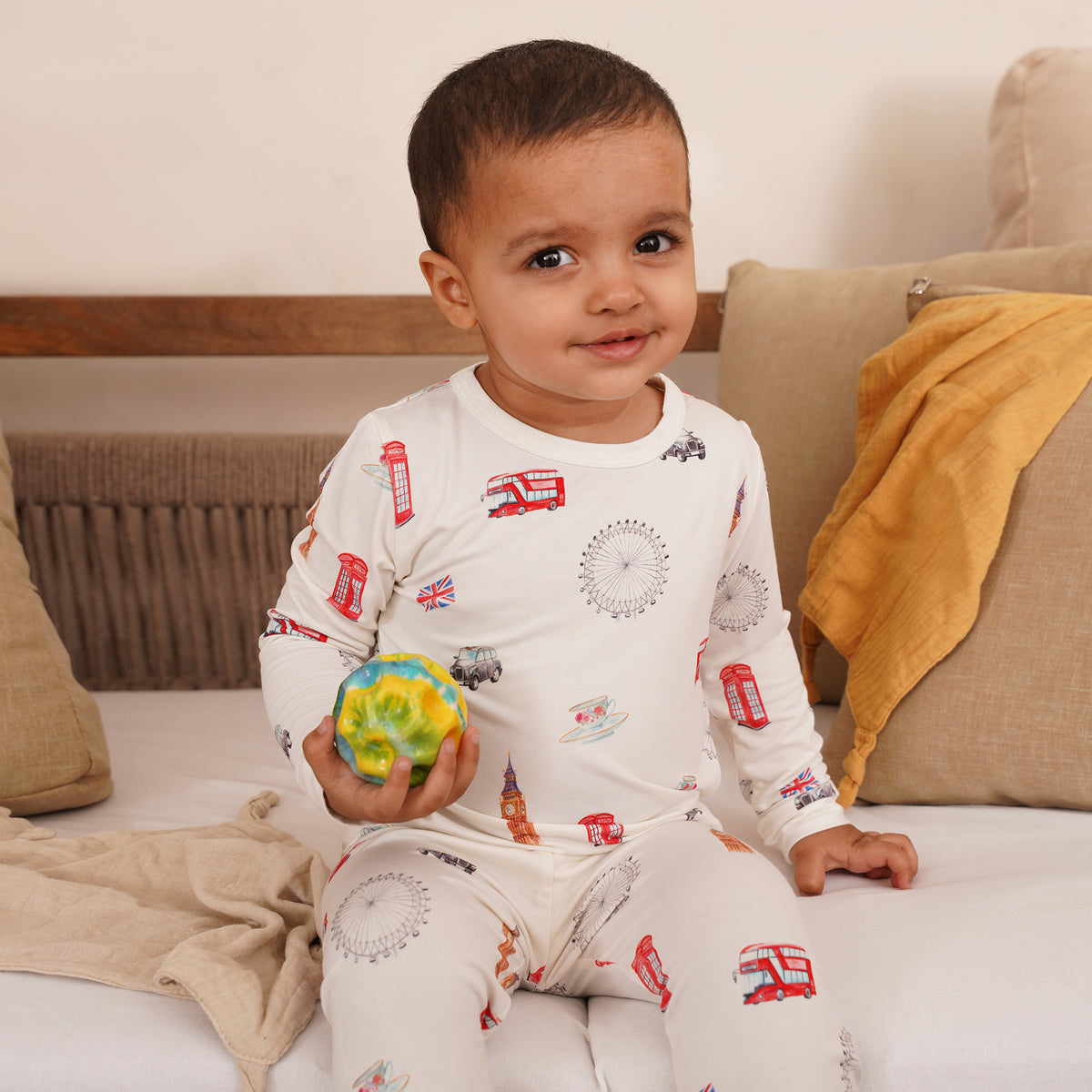 Child wearing a patterned outfit sitting on a couch holding a colorful ball.