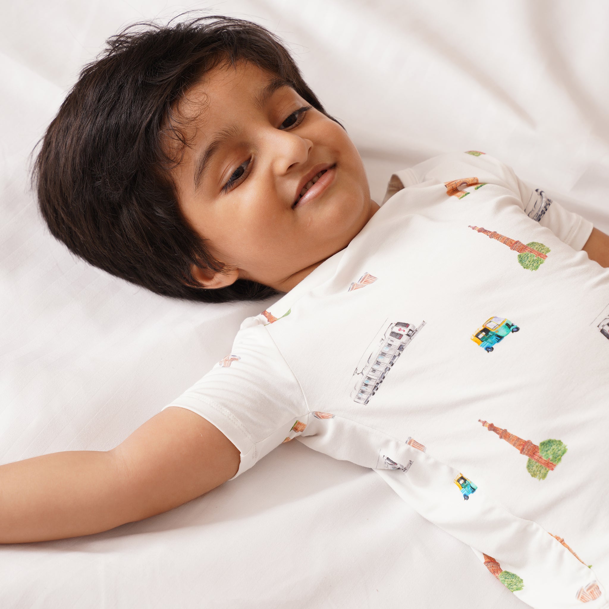 Child wearing a bamboo white shirt with colorful patterns lying on a white surface