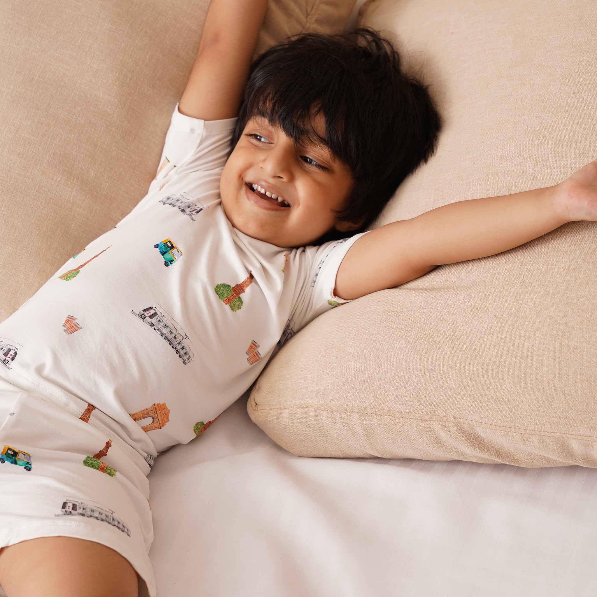 Child wearing a white bamboo shirt with colorful patterns, lying on a beige couch.