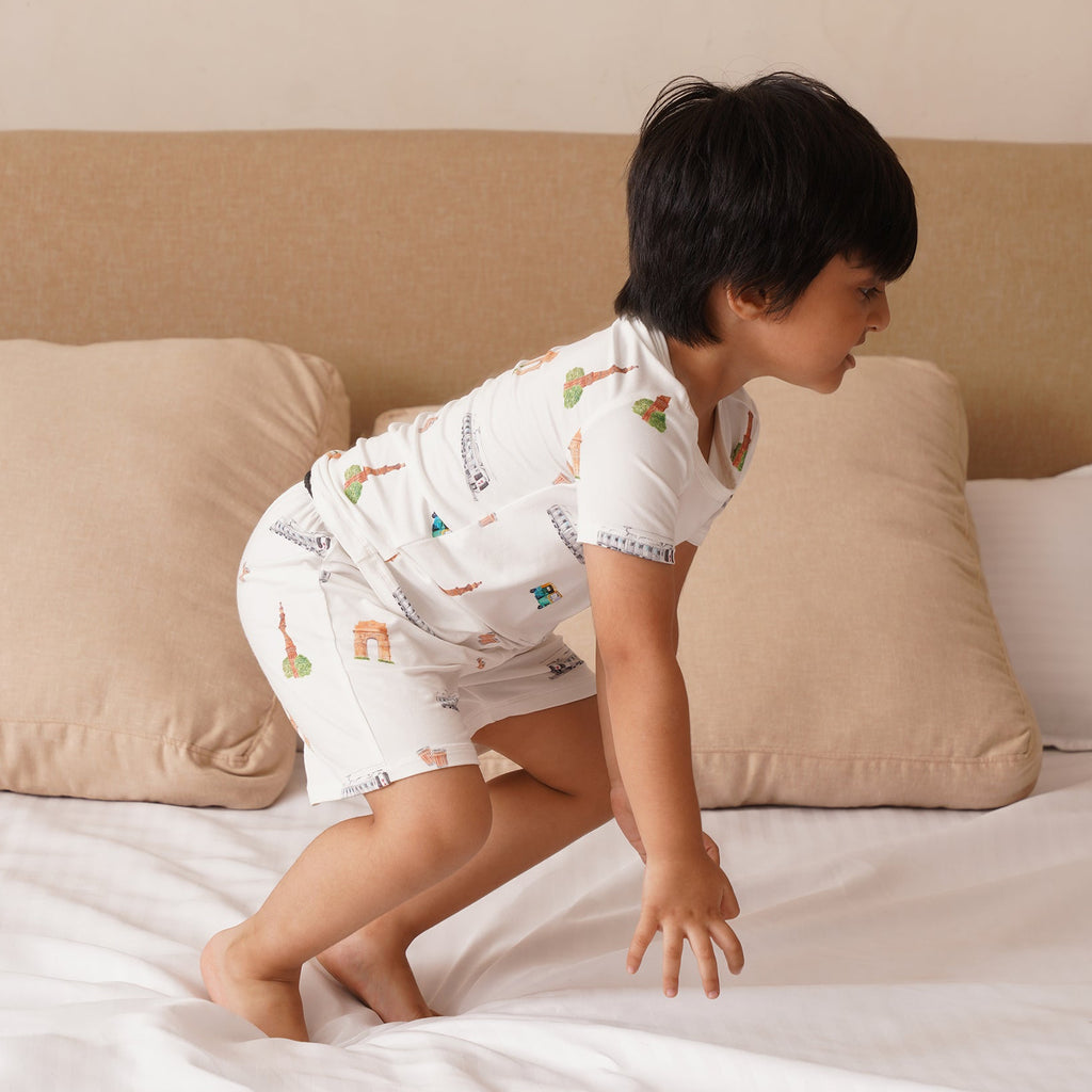 Child in bamboo pajamas standing on a bed with beige pillows and a neutral headboard.