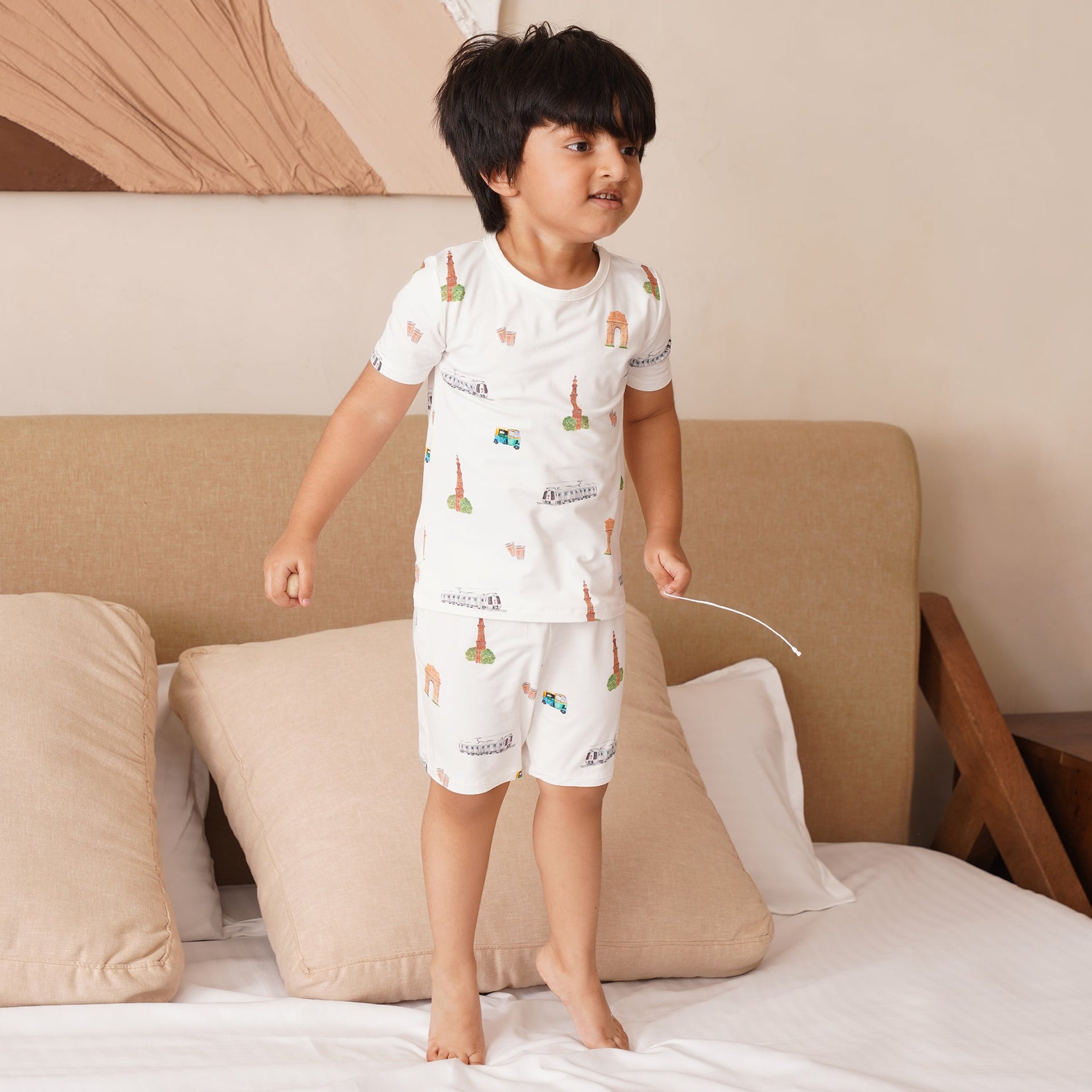 Child wearing a bamboo white pyjamas with colorful patterns standing on a bed.