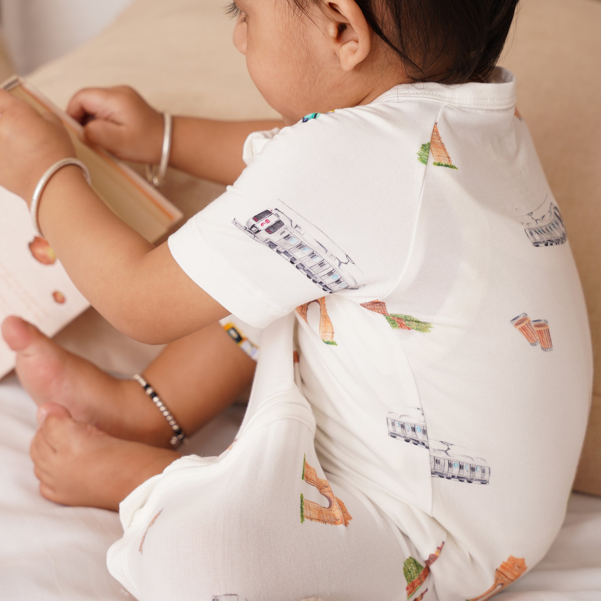 Child wearing a bamboo white shirt with colorful designs sitting on a bed.