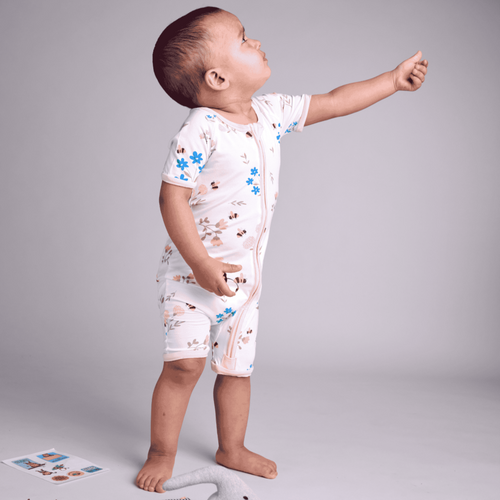 Child wearing a white onesie with colorful patterns, standing on a gray background with a toy elephant and books.