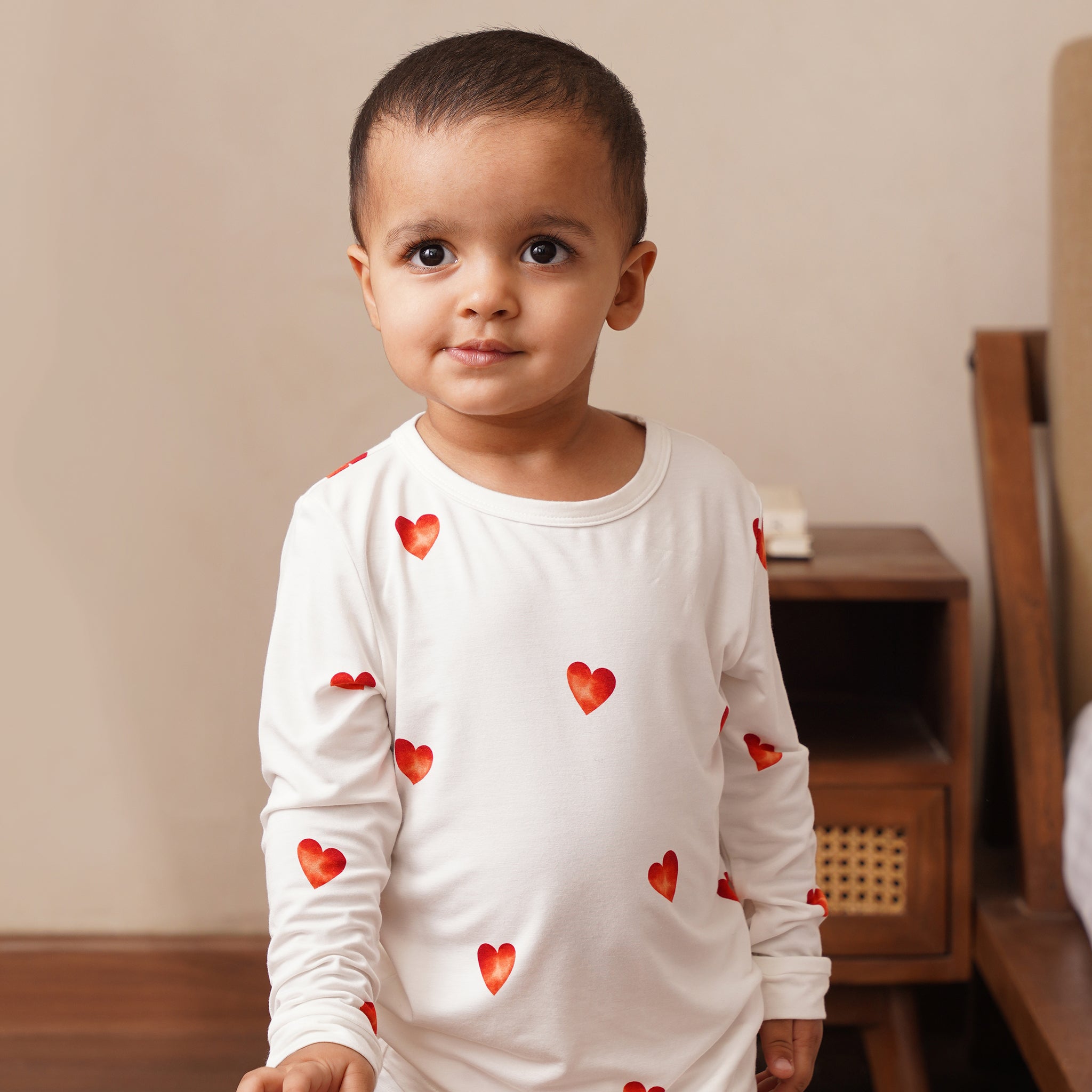 Child wearing a bamboo white long-sleeve shirt with red heart patterns in a room.