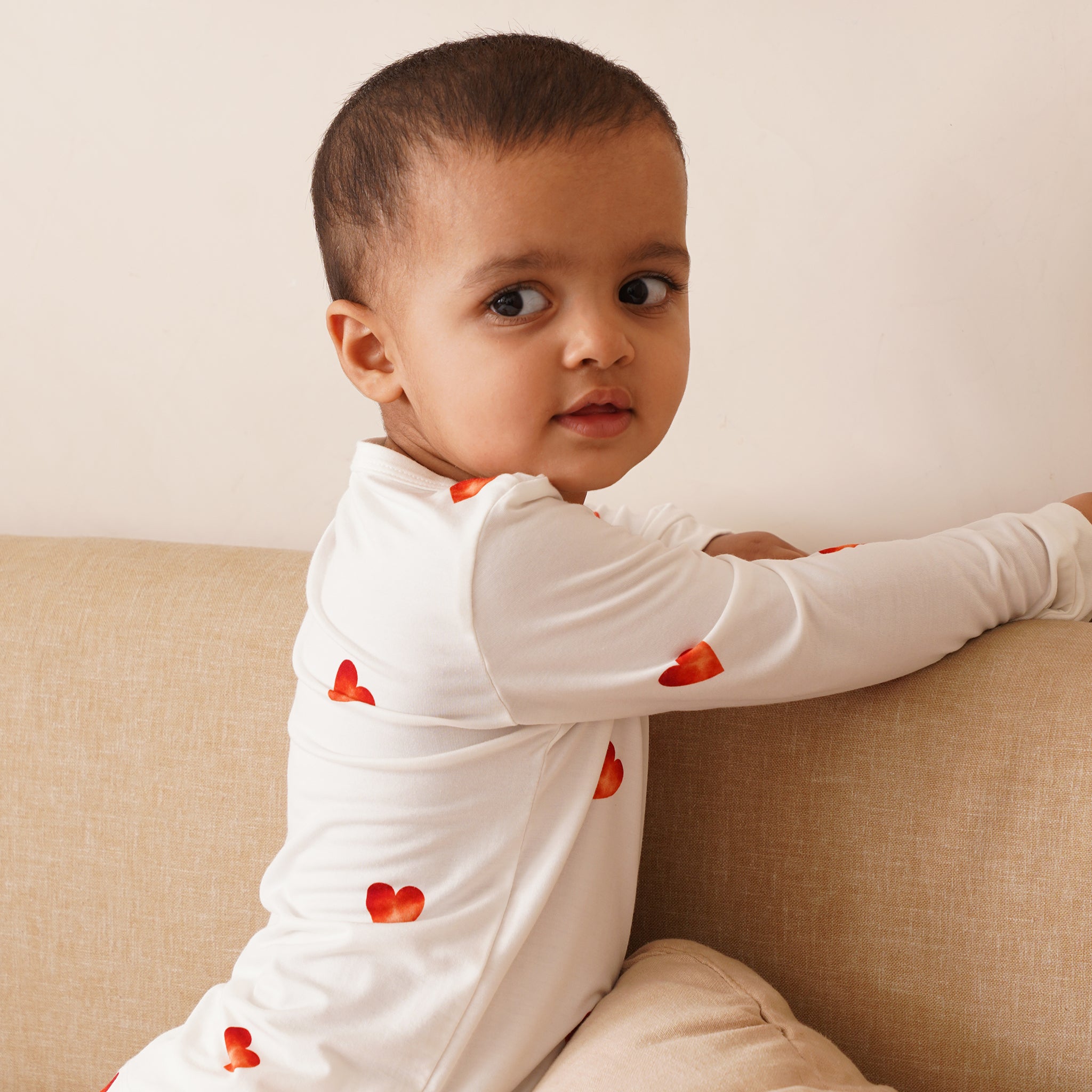 Child wearing a bamboo white long-sleeve shirt with red heart patterns, sitting on a beige couch.