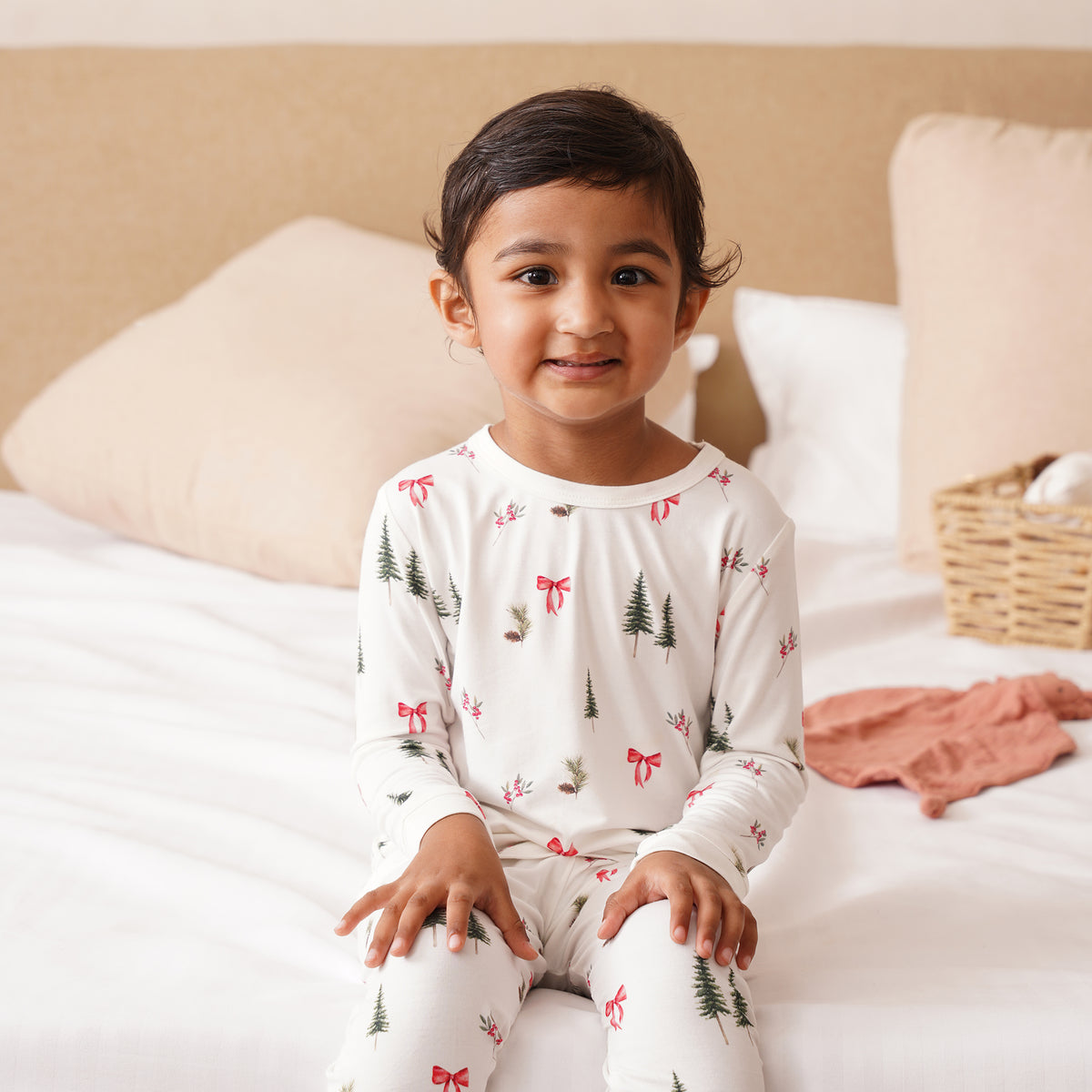 Child wearing bamboo pajamas with a Christmas tree and bow pattern, sitting on a bed.