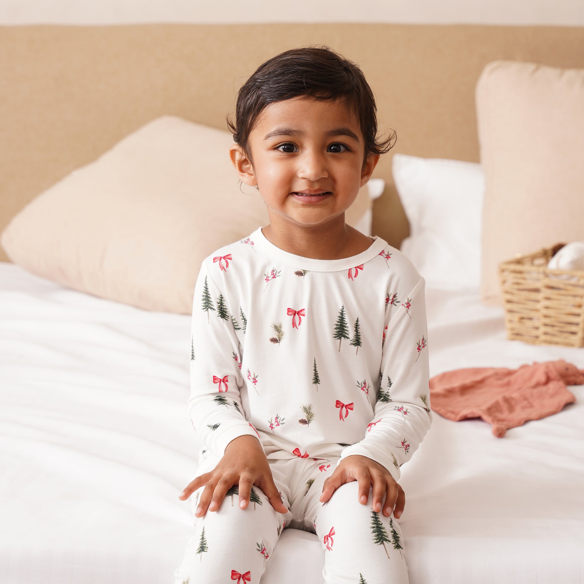 Child wearing bamboo pajamas with a Christmas tree and bow pattern, sitting on a bed.