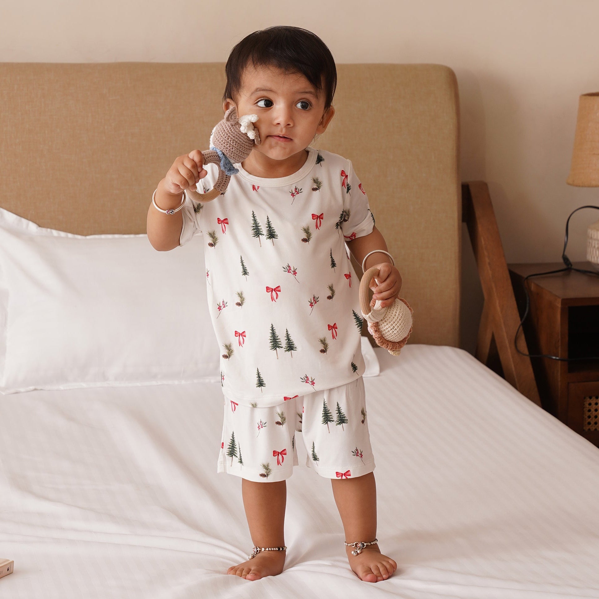 Child in bamboo pajamas holding baby rattles on a bed