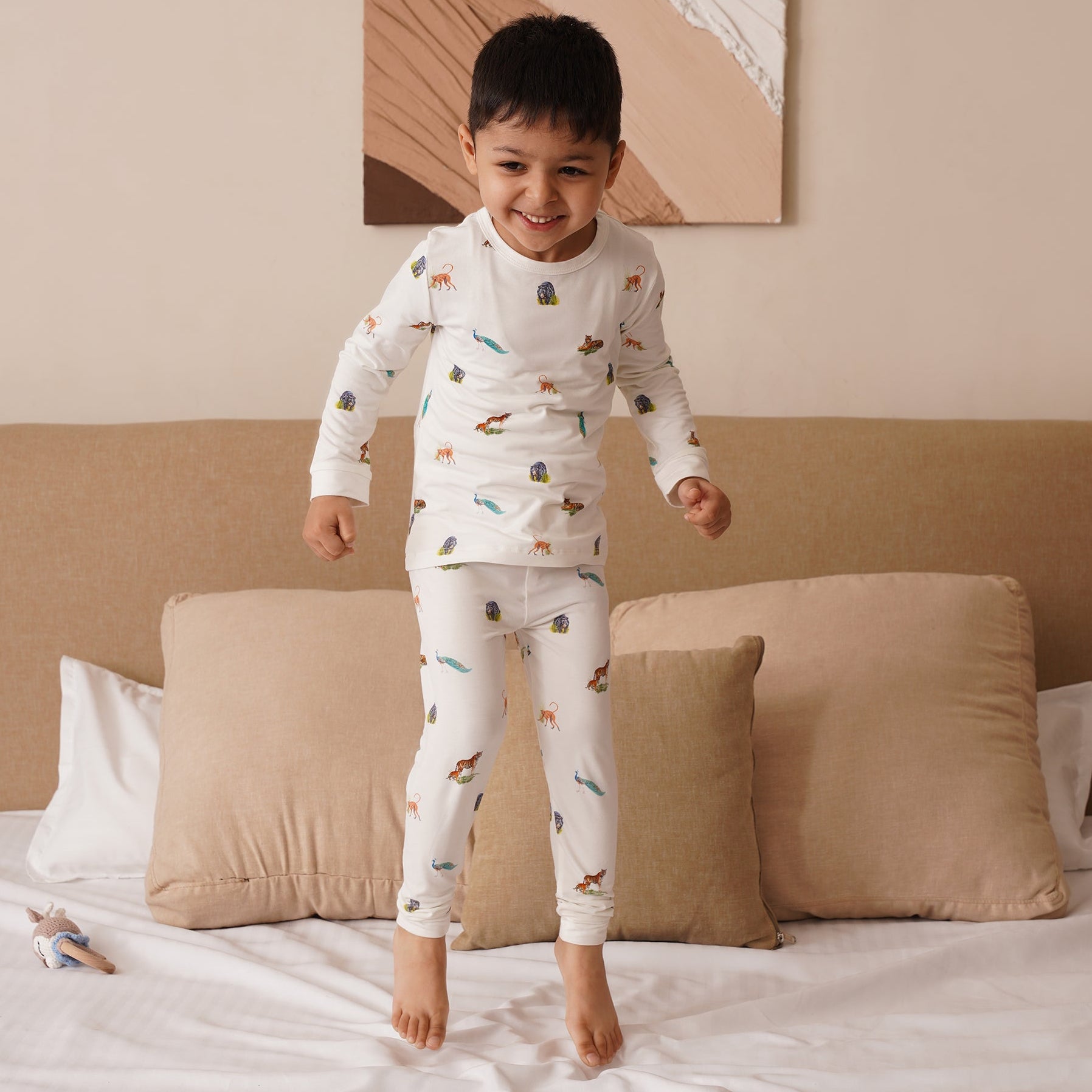 Child in bamboo pajamas standing on a bed in a bedroom