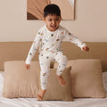 Child in bamboo pajamas jumping on a bed with a neutral-colored wall and abstract art in the background