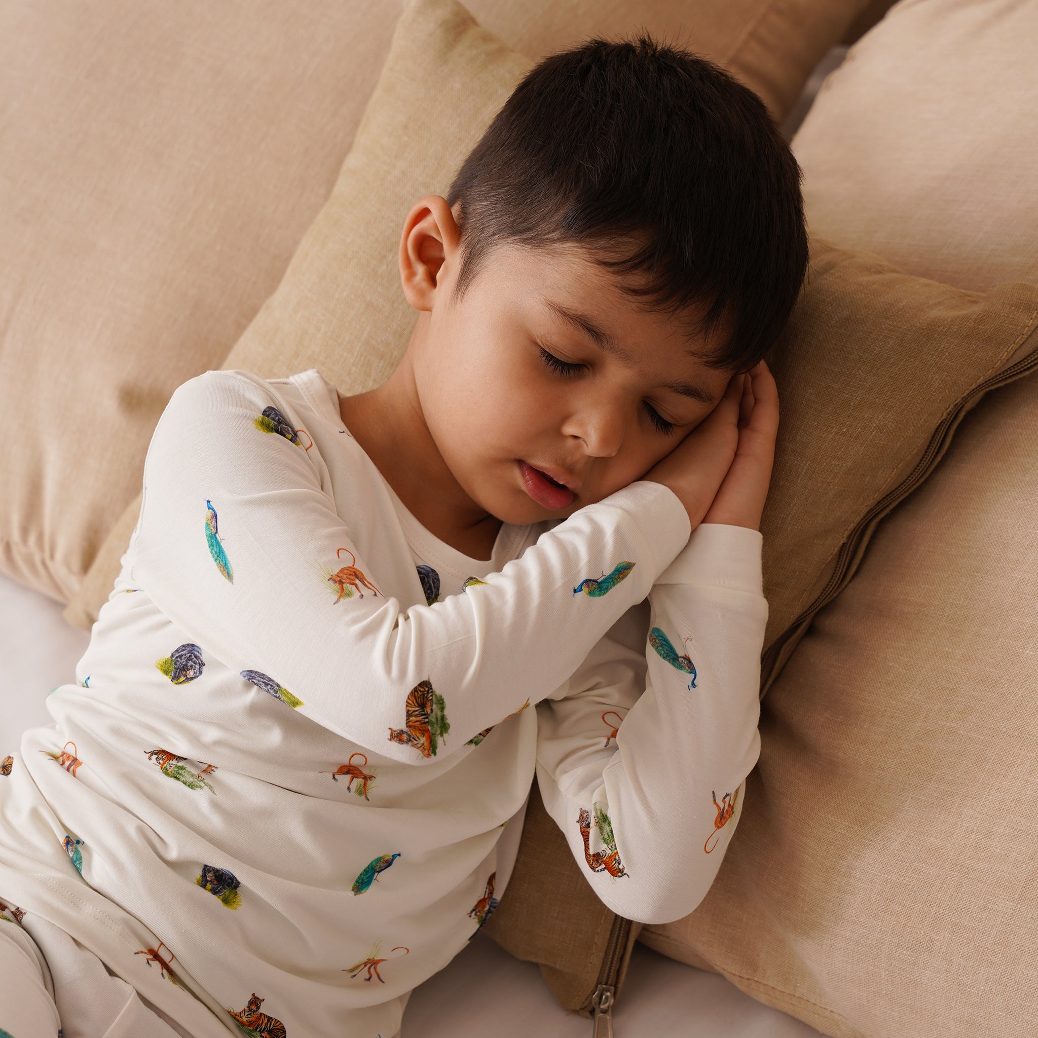 Child wearing bamboo pajamas with animal patterns, lying on a beige couch.