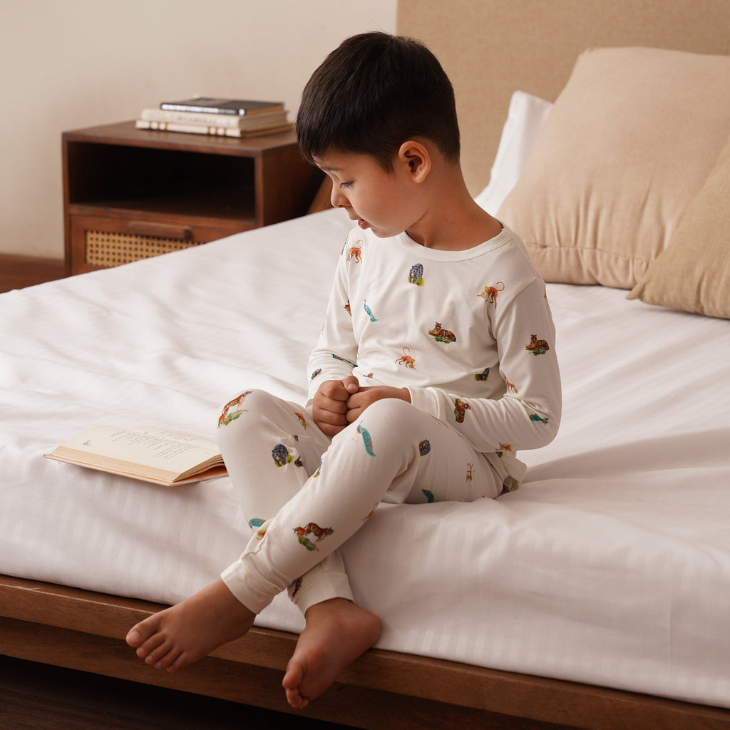 Child sitting in bamboo set on a bed reading a book in a cozy bedroom setting.