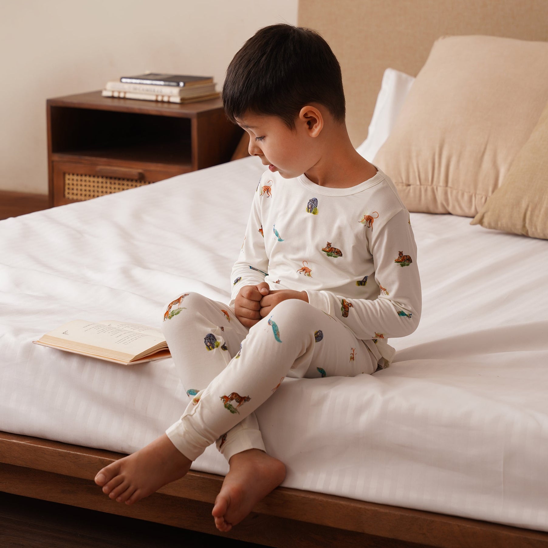 Child sitting in bamboo set on a bed reading a book in a cozy bedroom setting.