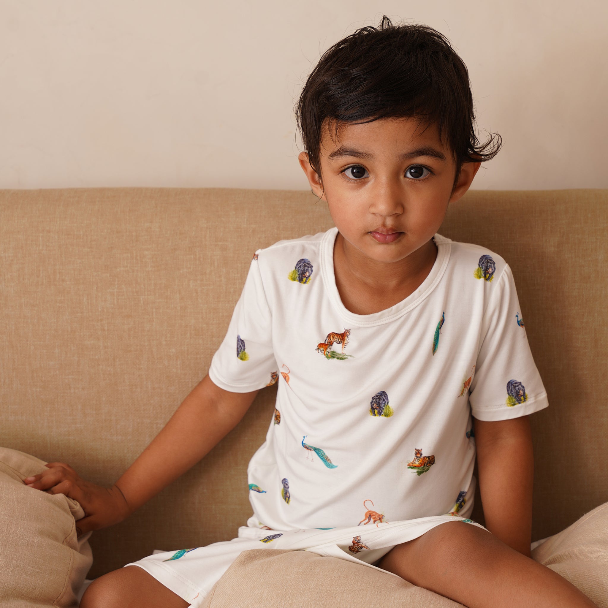 Child wearing a white bamboo t-shirt with colorful animal prints sitting on a beige couch.