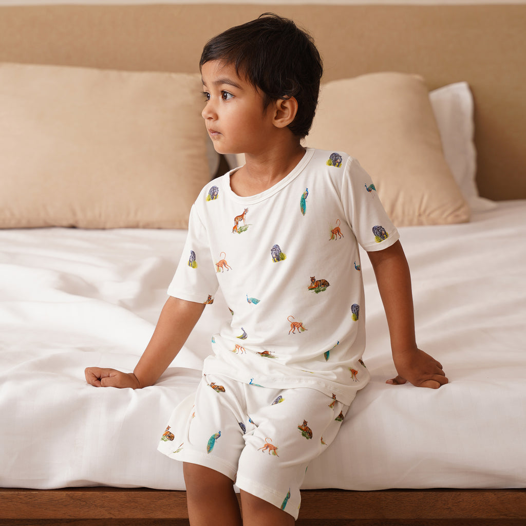 Child wearing a white bamboo pajama set with animal prints sitting on a bed.