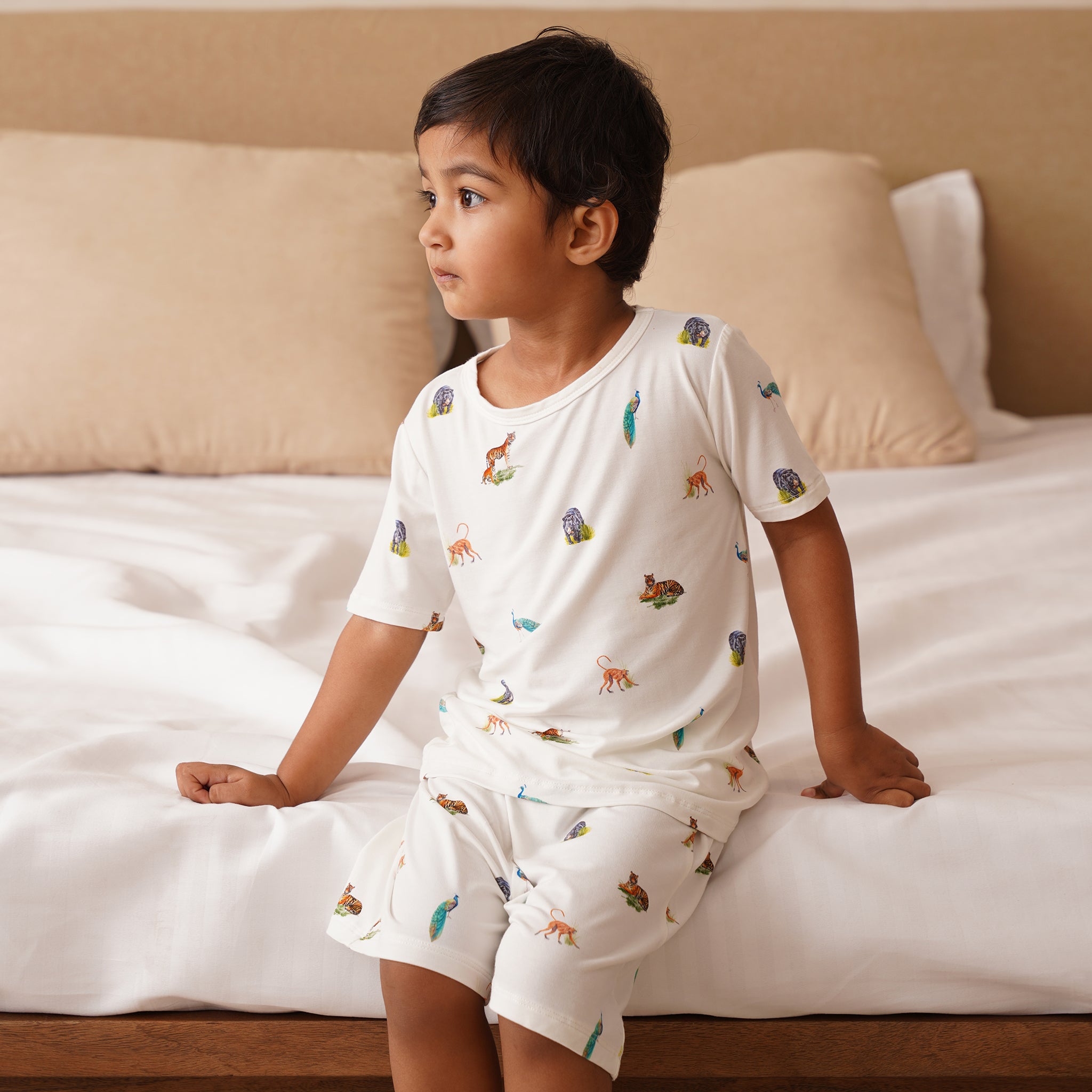 Child wearing a white bamboo pajama set with animal prints sitting on a bed.
