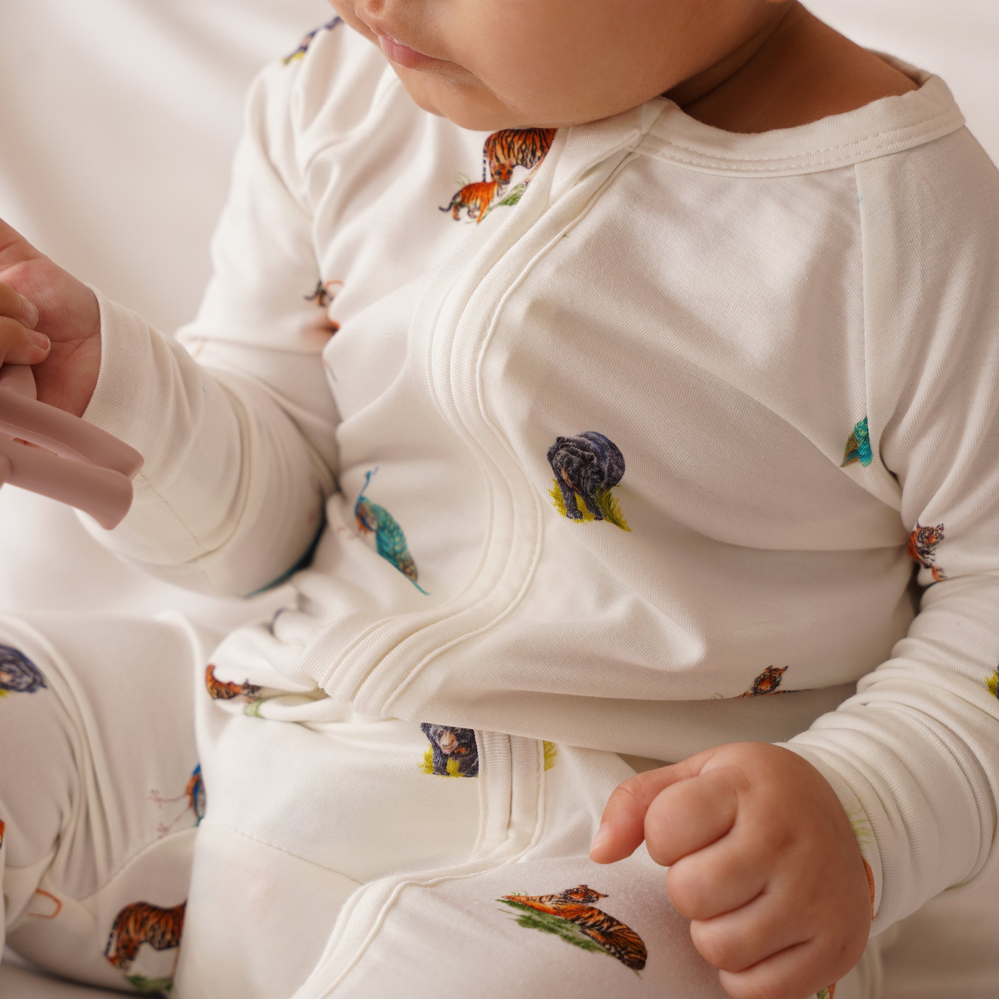 Close-up of a baby wearing a bamboo white onesie with animal prints on a plain background