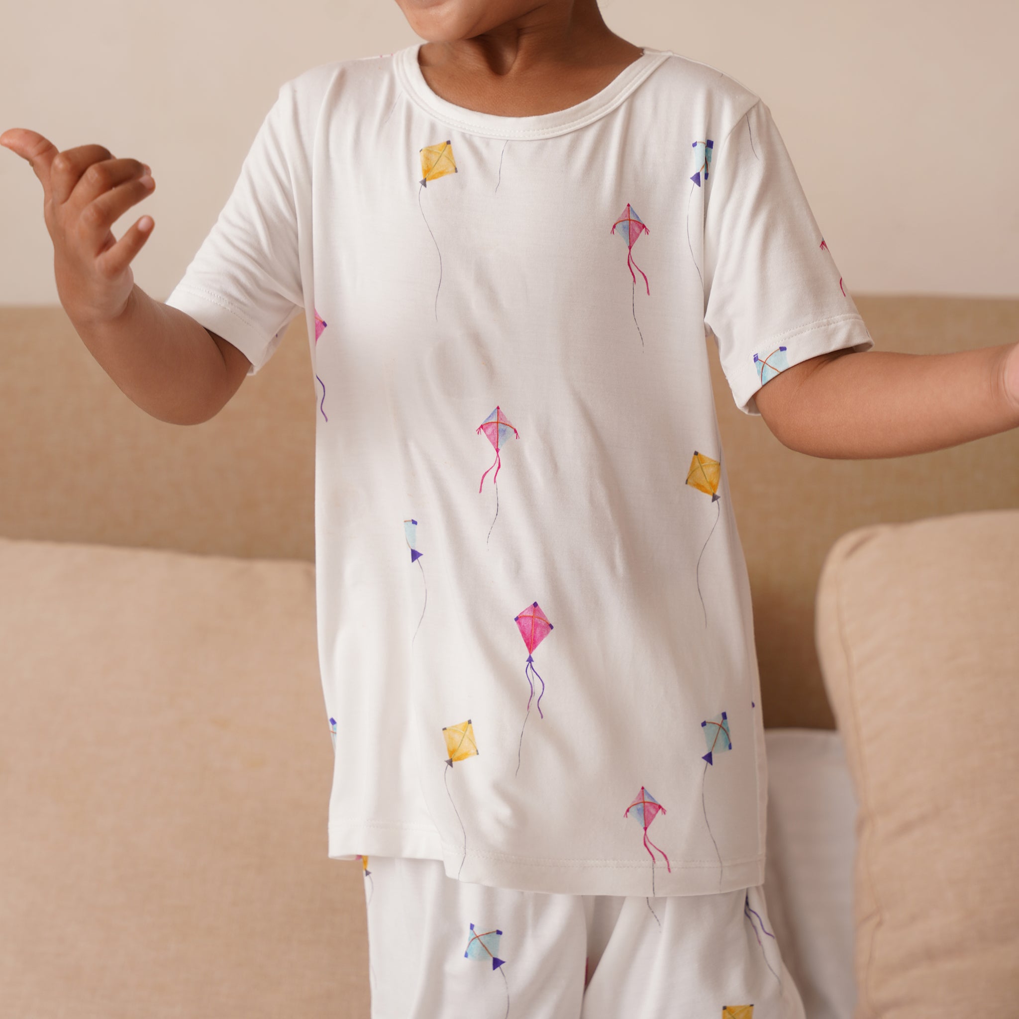Child wearing a white bamboo pajama set with colorful kite patterns on a beige couch.