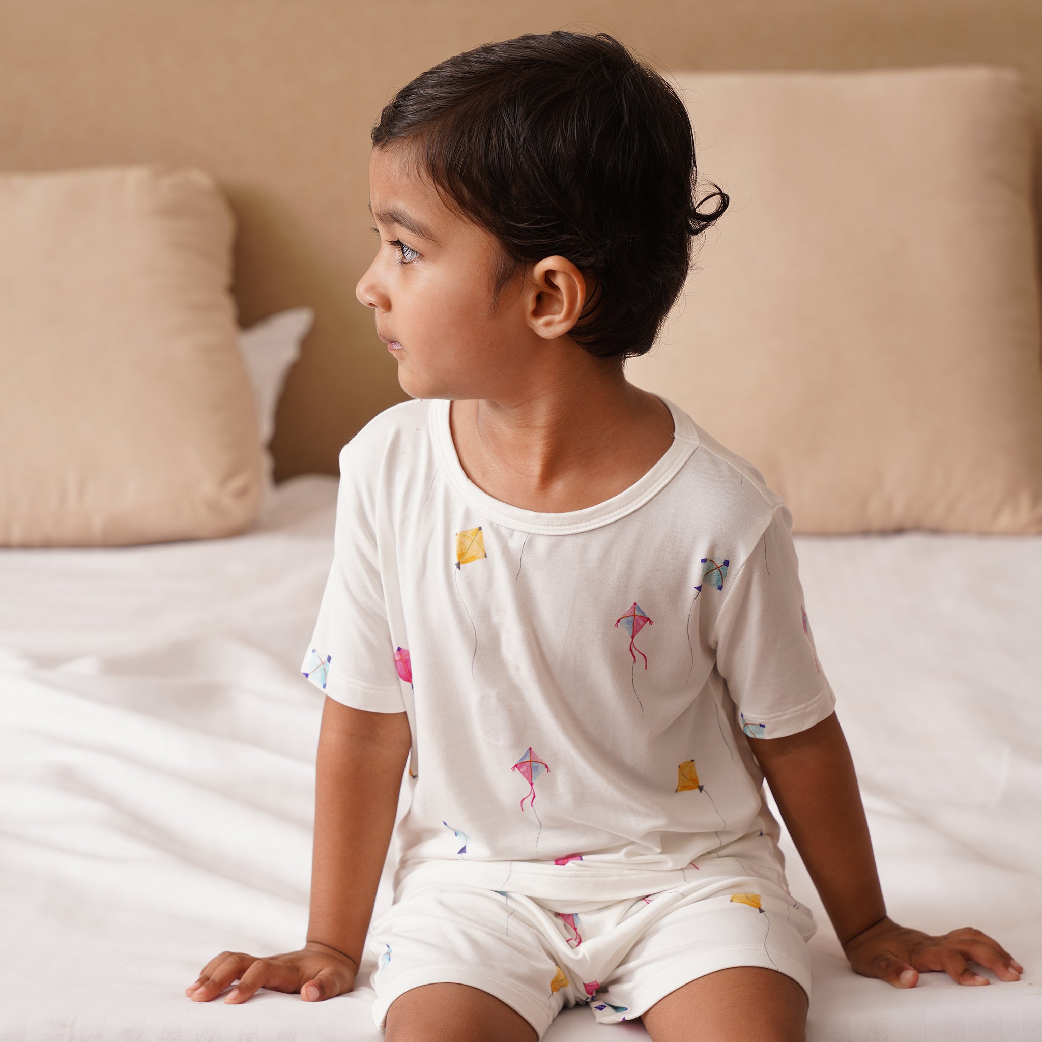 Child wearing a white bamboo pajama set with colorful designs sitting on a bed.