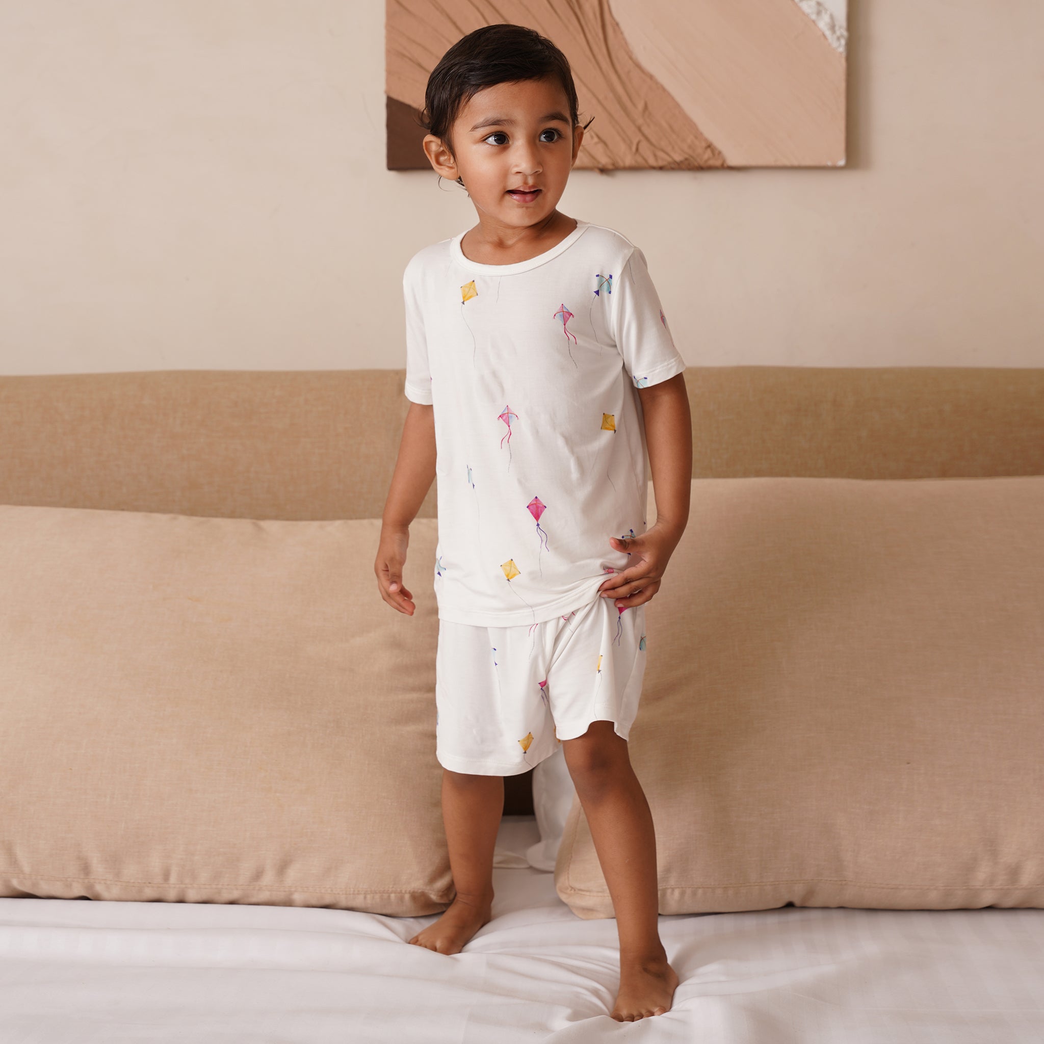 Child wearing a white bamboo pajama set with colorful designs standing on a bed.
