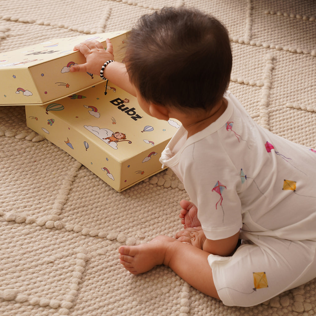 Child opening a yellow box with cartoon designs on a textured surface, wearing bamboo shortie