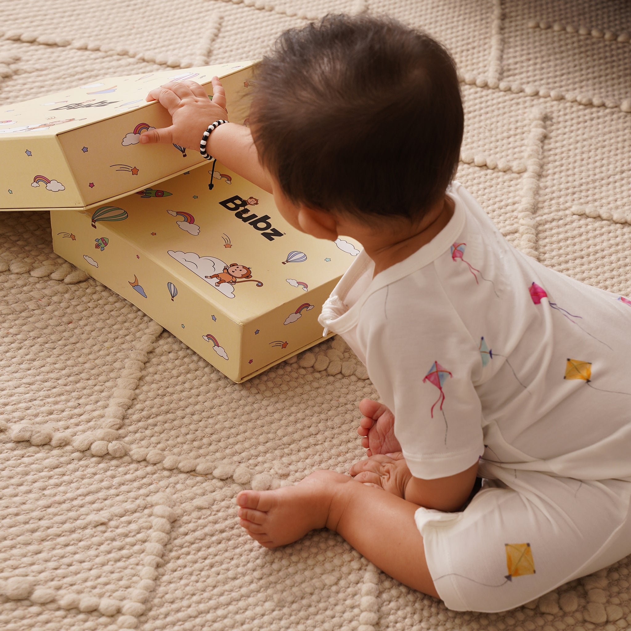Child opening a yellow box with cartoon designs on a textured surface, wearing bamboo shortie