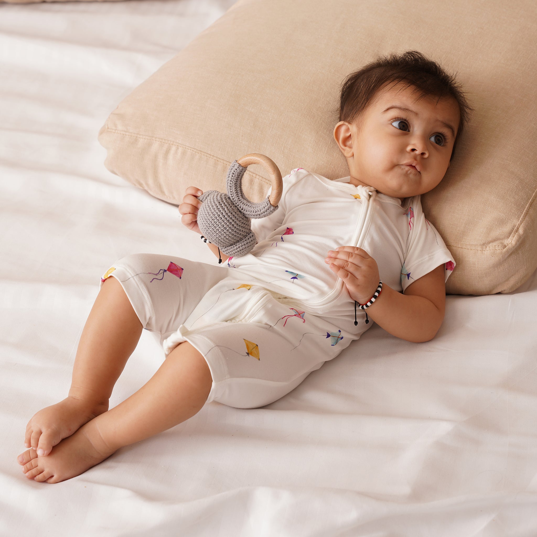 Baby lying on a bed holding a teething toy, wearing bamboo shortie