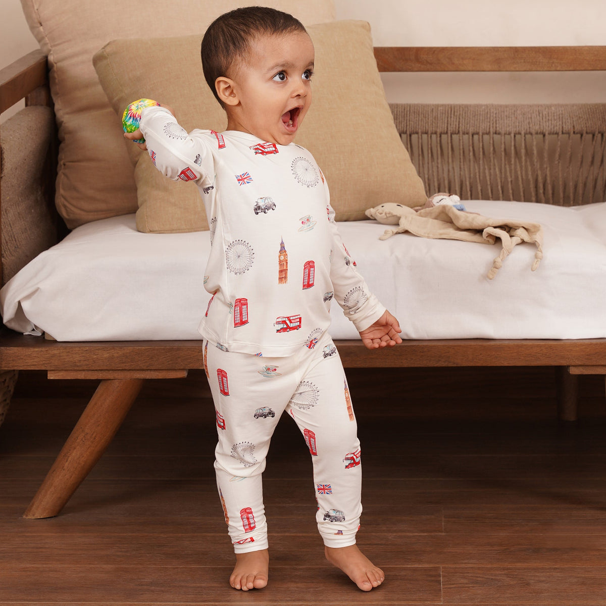 Child in bamboo pajamas with car pattern standing on a wooden floor, holding a toy.