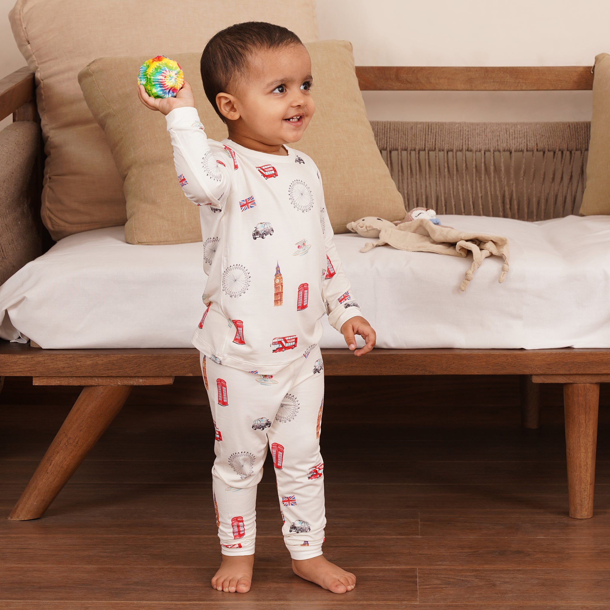 Child in bamboo pajamas standing on a wooden floor holding a colorful toy.