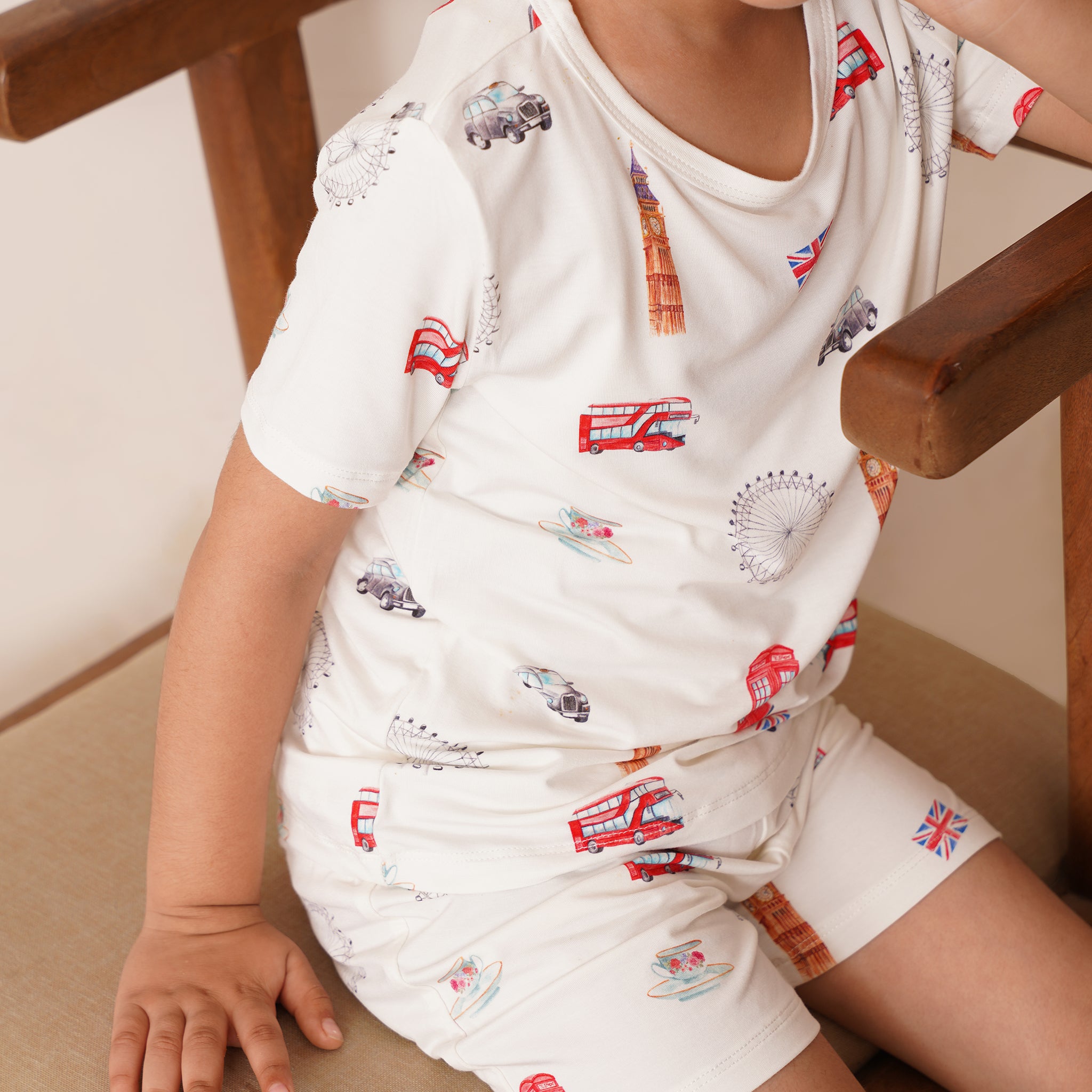 Child wearing a bamboo white outfit with red and blue graphics sitting on a wooden chair.
