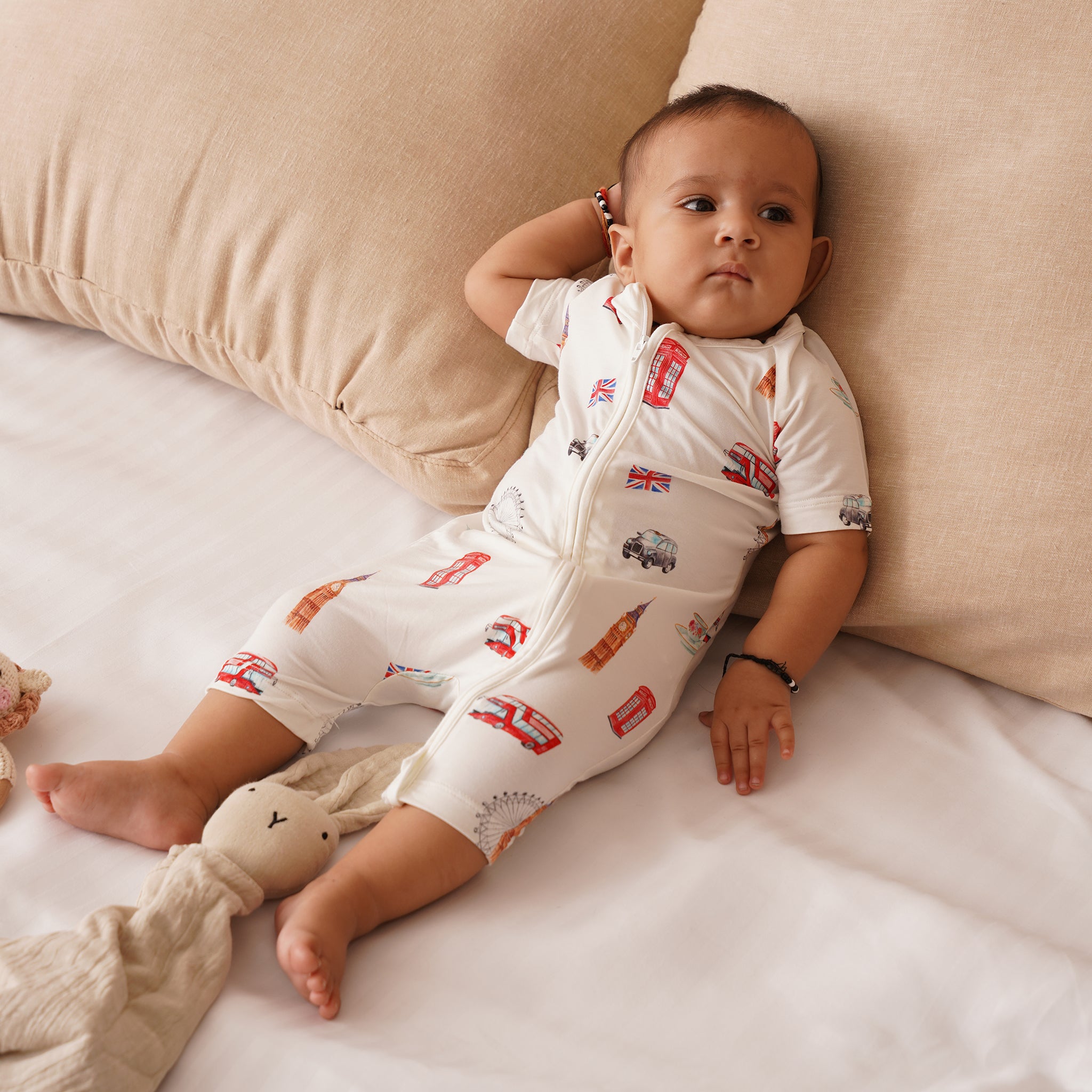 Baby wearing a white bamboo onesie with red and brown graphics, sitting on a beige couch.