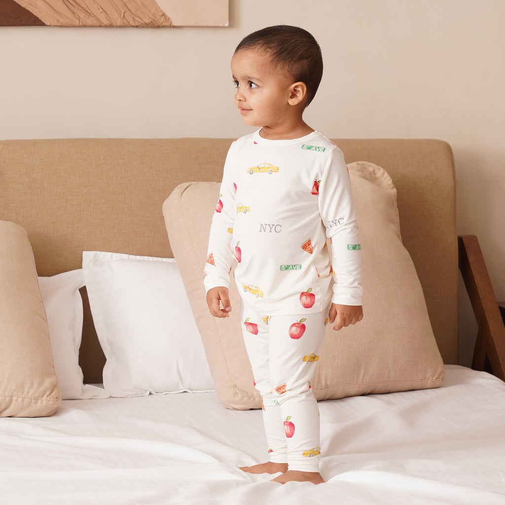 Child wearing a white bamboo pajama set with fruit patterns on a bed.