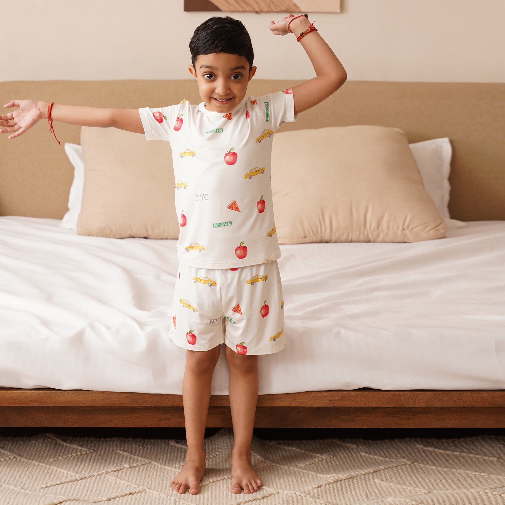 Child wearing a bamboo pajama set with fruit patterns standing in front of a bed.