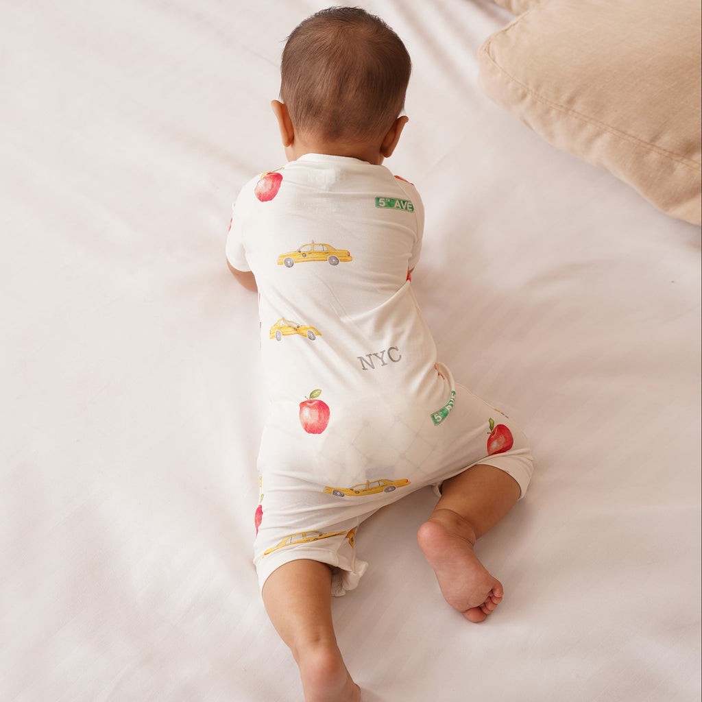 Baby wearing a white bamboo onesie with colorful prints on a light-colored surface