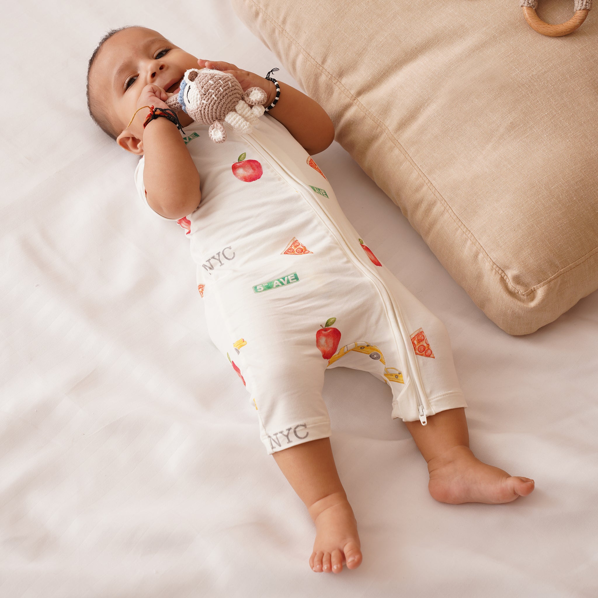 Baby lying on a white surface with a beige pillow and wooden toy in the background, wearing bamboo shortie