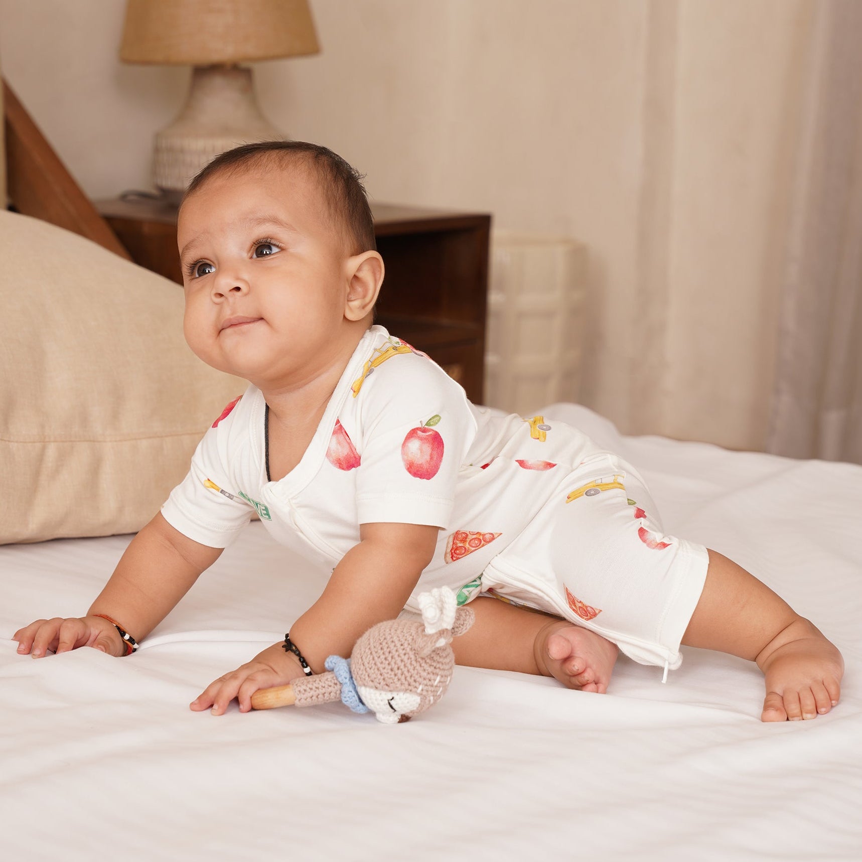 Baby in a white bamboo outfit with fruit patterns on a bed