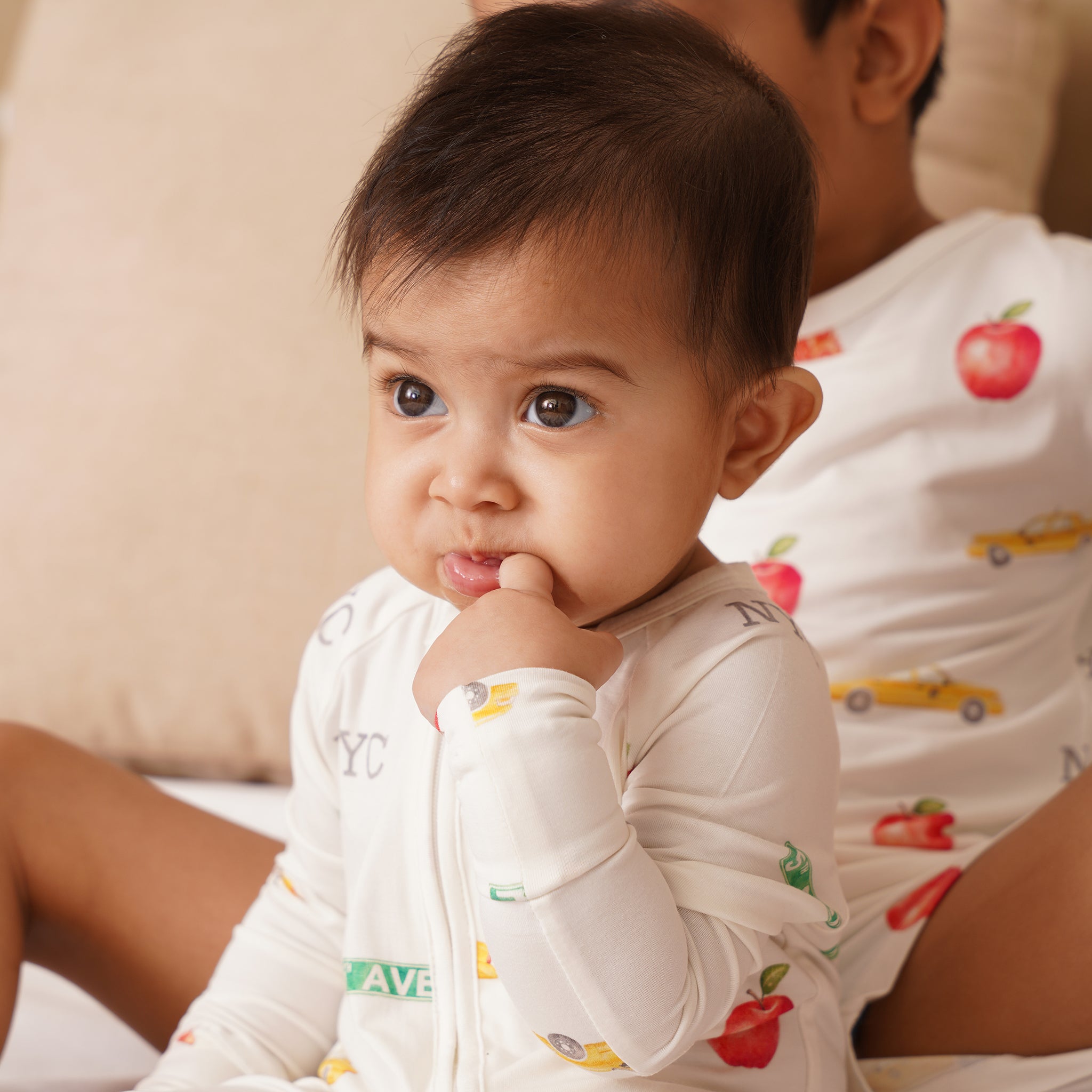 Baby wearing a white bamboo long-sleeve shirt with colorful patterns, sitting next to an adult.