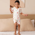 Child wearing a white  bamboopajama set with fruit patterns on a bed.